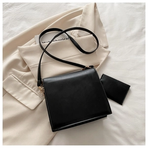 Sac bandoulière en cuir noir mat avec porte-cartes assorti sur un blazer beige chic