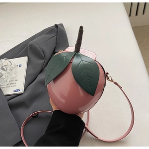 Détail d'un sac bandoulière rose en forme de pêche avec décor de feuilles et cuir brillant