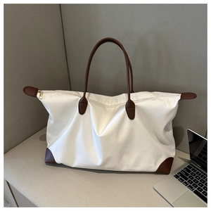 Bolso de viaje grande blanco de nailon con asas marrones junto a un portátil.