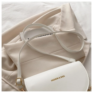 Détail d'un sac à main blanc en cuir avec lettrage doré posé sur une veste beige