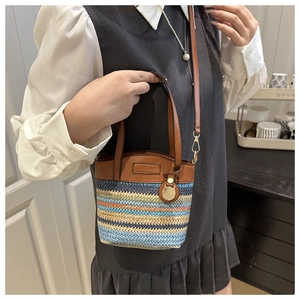 Close-up of a striped straw bucket bag with brown leather handles and a woven texture