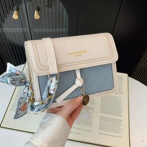 Detail of bicolor crossbody bag with silk scarf charm and gold logo lettering