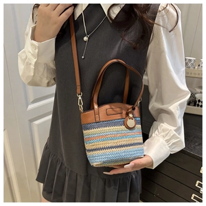Detail of colorful woven straw bucket bag with brown faux leather handles and strap