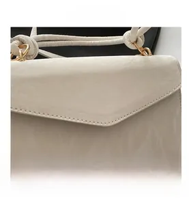 Detailed close-up of cream textured pleated leather handbag with knotted strap and gold rings