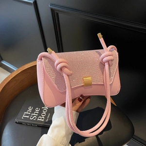 Pink baguette bag with glitter flap and knot shoulder strap shown on a dark chair