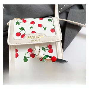Detailed close-up of white crossbody bag with red cherry prints and decorative charm