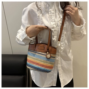 Detail of colorful woven bucket bag with brown leather strap worn by a model