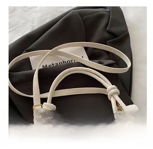 Detail of dual shoulder straps with golden buckles and knot on white leather bag