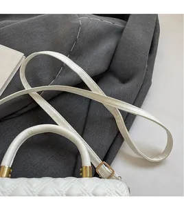 Detail of white quilted crossbody bag with golden hardware and adjustable long shoulder strap