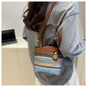 Detail of multi-color woven straw bucket bag with brown leather trim and gold metal hardware