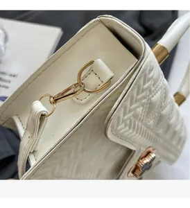 Close-up of white embossed cross-pattern bag with elegant gold floral clasp and metal hardware
