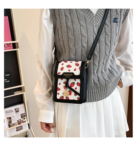 Detail of white mini crossbody bag with red strawberry print and black leather trim