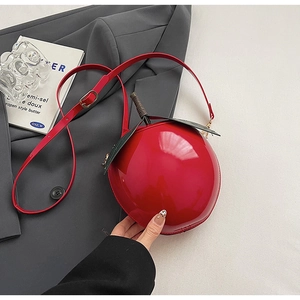 Détail du sac bandoulière cerise rouge avec feuille verte et finition vernie brillante