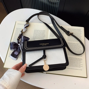 Close-up of contrast crossbody bag with gold lettering, leather texture, and silk scarf