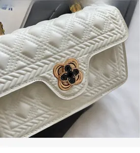 Detail view of the golden floral clasp and quilted leather texture on the white bag