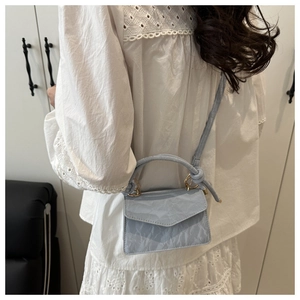 Detailed side view of a light blue pleated handbag with golden buckle on a white dress