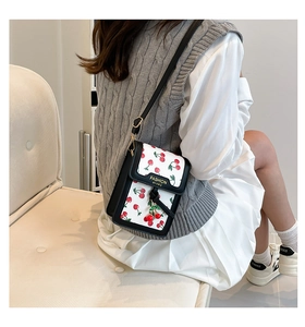 Detail of white leather crossbody bag with cherry prints and a cute cherry pendant charm