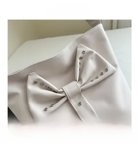 Detail shot of a cream leather tote bag featuring a bow with sparkling silver rhinestones