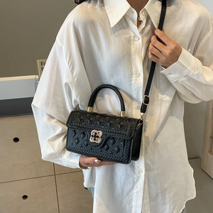 Detail of black quilted shoulder bag with gold clover lock and textured leather finish