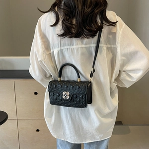 Detail of black quilted shoulder bag with gold clover lock on a crossbody strap