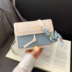 Detail of light blue crossbody bag with white flap, silk scarf and gold charm pendant
