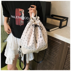 Detail of a beige drawstring bucket bag with bow patterns and durable black leather base