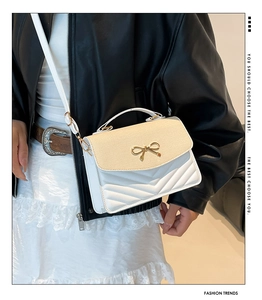 Detail of crossbody bag with woven flap, gold bow accent and V-quilted texture