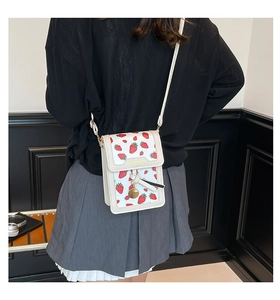 Detail of white crossbody bag with red strawberry print and golden charm on a model