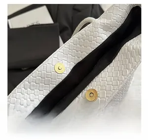 Close-up of golden magnetic buckle on white woven leather tote bag with black lining