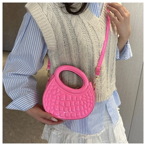 Close-up of a vibrant pink round handbag with crocodile texture worn by a model