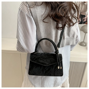 Detail of black textured handbag with curved handle shown in a minimalist setting