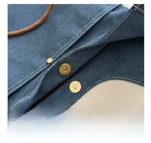 Detail of blue denim tote featuring gold magnetic snap closure and woven rope handle