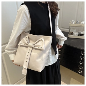 Detail of off-white tote bag featuring a large bow and metallic stud accents on the front