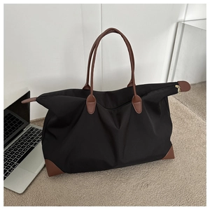 Bolsa de viaje de nailon negro de gran capacidad con asas de cuero marrón en un escritorio