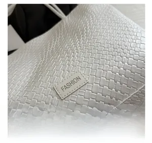 Close-up of white woven leather texture with a stitched FASHION label on the tote bag