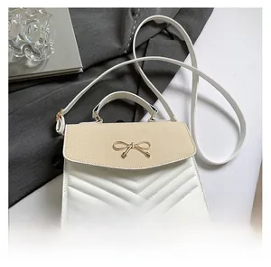 Detail of V-quilted faux leather crossbody bag with golden bow clasp and woven texture