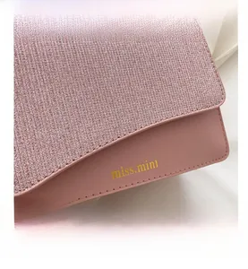 Dettaglio della patta con paillettes rosa e logo dorato sulla borsa a tracolla