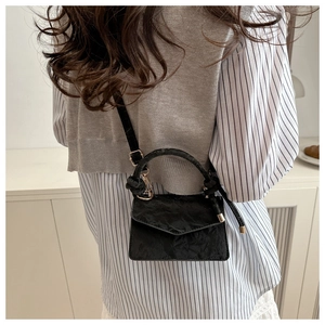 Detail of black pleated crossbody bag with chunky handle and gold hardware on model