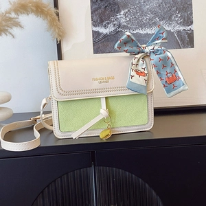 Detail of green and beige crossbody bag featuring polka dot stitching and floral silk scarf