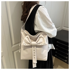 Close-up of cream tote bag with large bow detail and metallic studs worn by a model