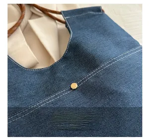 Detail of blue denim fabric with white stitching, metal rivet and woven rope handle
