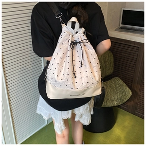 Detail of cream drawstring bucket bag featuring black bow patterns and textured fabric
