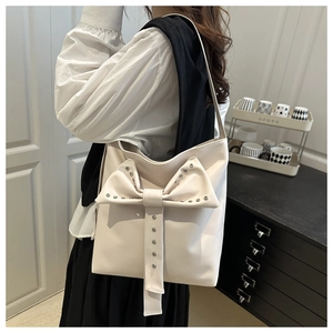 Detail of cream shoulder bag with large bow and metal rivets on model in modern room