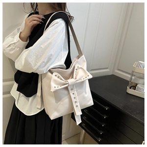 Close-up of white hobo bag featuring large bow decoration and silver metal rivets
