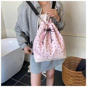 Detail of pink drawstring bag featuring black ribbon bow patterns and printed logo text