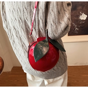 Sac bandoulière en forme de pomme rouge en cuir verni brillant porté sur un pull gris