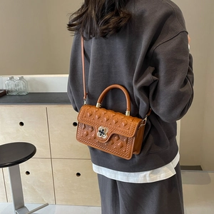 Detail shot of caramel quilted handbag featuring an elegant clover metal clasp design