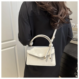 Detail of stone-textured cream crossbody bag featuring a unique knot handle and metal strap