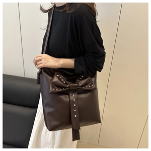 Detailed view of deep brown tote bag featuring a large bow and silver metal rivets