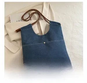 Detail showing the denim fabric texture, rope handle, and metal button of the tote bag